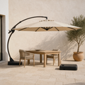 In a room | warm limestone terrace with Sand offset cantilever umbrella, dining table and two chairs beneath the canopy, separate wheeled base at right