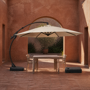 In a room | terracotta courtyard with Sand offset cantilever umbrella, square table and chairs beneath the canopy, separate wheeled base at right