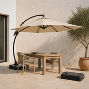 Warm limestone terrace view of the complete Sand umbrella and separate wheeled base beside a dining table