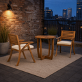 On a roof terrace | two cream-cushioned acacia armchairs and the round table at blue hour