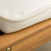 Macro | cream cushion weave and piping beside the acacia seat rail and brass-toned fastener