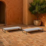 Angle | two flat pale-gray mesh chaise lounges on a terracotta garden loggia