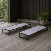 Room | two flat pale-gray mesh chaise lounges on a cedar deck beside a fern