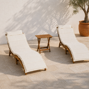 Terrace three-quarter view of two ivory-cushioned acacia chaise lounges and folding side table