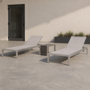 In scale | full chaise lounge set beside an uncropped black exterior doorway on a concrete patio