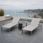 Coastal terrace | two light gray mesh chaise lounges and side table on blue-gray slate above the ocean