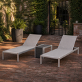 Garden courtyard | two light gray chaise lounges and woven side table on red brick beneath ivy