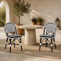 In a room | two black-and-white woven bistro dining chairs at a round stone patio table on a sunlit courtyard