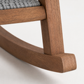 Hardware | macro view of the curved eucalyptus rocking runner joint beside gray woven resin wicker