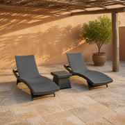 In a room | two charcoal-gray woven chaise loungers and a matching side table in a terracotta courtyard