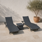 Complete set of two charcoal-gray woven chaise loungers and one matching side table on a limestone terrace