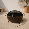 Angle | sunlit limestone terrace three-quarter view of bronze fire pit with mesh screen and poker
