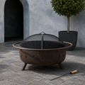 In a room | cool slate courtyard view of bronze fire pit with mesh screen seated and poker at right