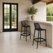 In scale | two black lattice bar stools beside a tall black-framed glass doorway at a pale outdoor bar