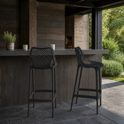 In a room | two black lattice bar stools at a charcoal covered bar, with dark wood wall and brick opening