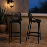 In a room | two black lattice bar stools on terracotta pavers beside a stucco bar at blue hour