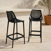 Set | two black lattice bar stools at a pale terrace bar, one front-facing and one turned to show its side profile