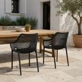 Terrace dining | two matte-black open-mesh armchairs at a teak table on a limestone patio