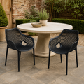 Garden courtyard | two matte-black open-mesh armchairs at a round stone outdoor table